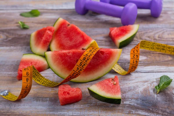 Fresh ripe watermelon slices, dumbbells and measuring tape on wooden background — Stock Photo, Image