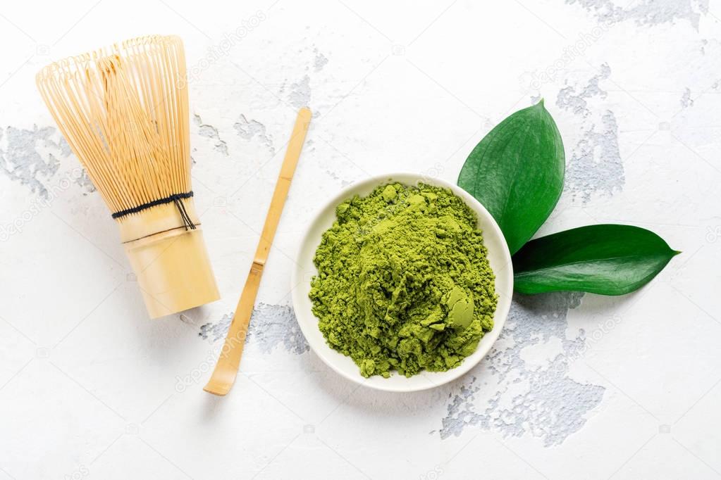 Green matcha tea powder and tea accessories on white background