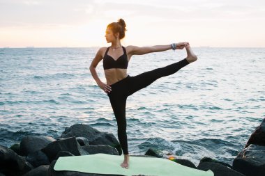 Pratik Yoga kayalık sahil, gündoğumu veya günbatımı genç kadın