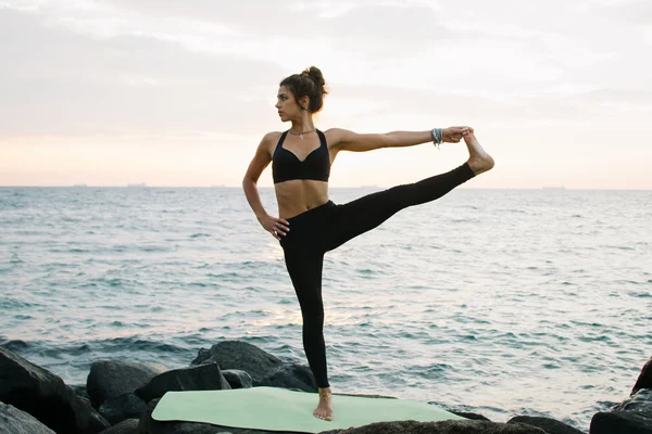 Mujer joven practicando yoga en la costa rocosa al amanecer o al atardecer — Foto de Stock