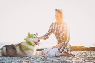 Genç erkek Sibirya husky köpek ile kumsalda güneş doğarken oynuyor.