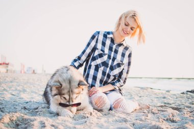 Genç erkek Sibirya husky köpek ile kumsalda güneş doğarken oynuyor.