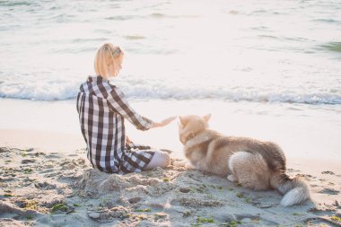 Genç erkek Sibirya husky köpek ile kumsalda güneş doğarken oynuyor.