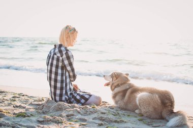 Genç erkek Sibirya husky köpek ile kumsalda güneş doğarken oynuyor.