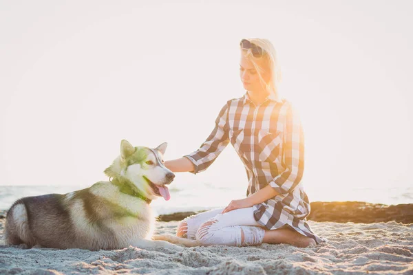 Jovem fêmea brincando com siberiano husky cão na praia ao nascer do sol — Fotografia de Stock