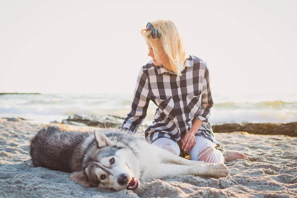 Молодая женщина играет с сибирской хаски-собакой на пляже на рассвете — стоковое фото