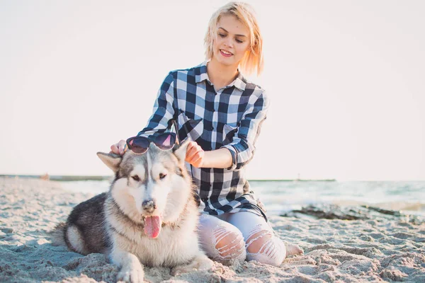 Jovem fêmea colocando óculos de sol no cão husky siberiano na praia — Fotografia de Stock