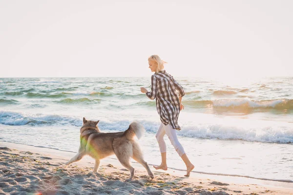 Jovem fêmea correndo com cão husky siberiano em frente ao mar ao nascer do sol — Fotografia de Stock
