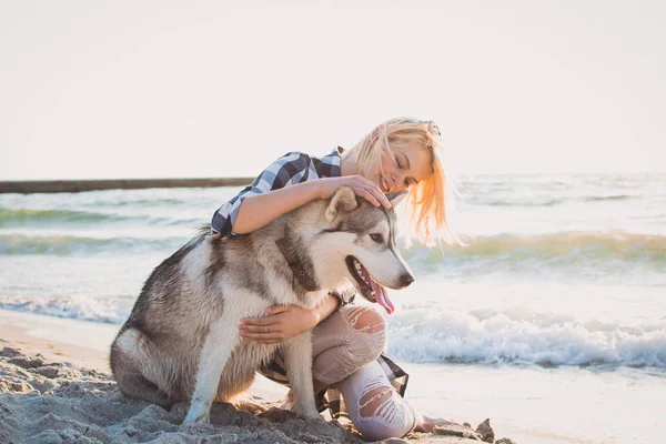 Mladá žena objímala s sibiřský husky psa na pláži při západu slunce — Stock fotografie