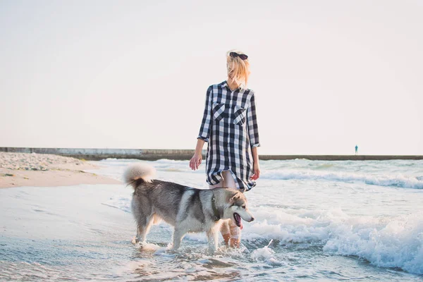 Jovem fêmea caminhando com cão husky siberiano em frente ao mar ao nascer do sol — Fotografia de Stock