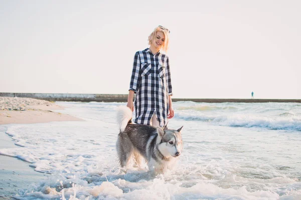 Jovem fêmea caminhando com cão husky siberiano em frente ao mar ao nascer do sol — Fotografia de Stock