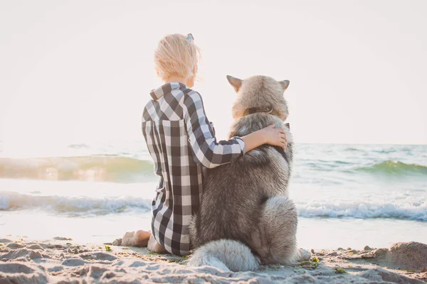 Młoda suczka przytulanie z psem husky syberyjski na plaży o wschodzie słońca — Zdjęcie stockowe