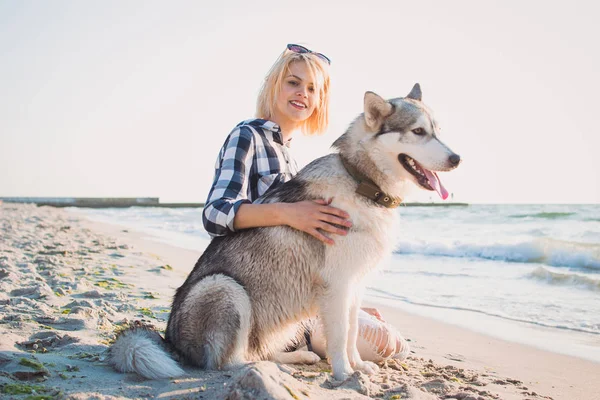 Молодая женщина обнимается с сибирской хаски-собакой на пляже на рассвете — стоковое фото