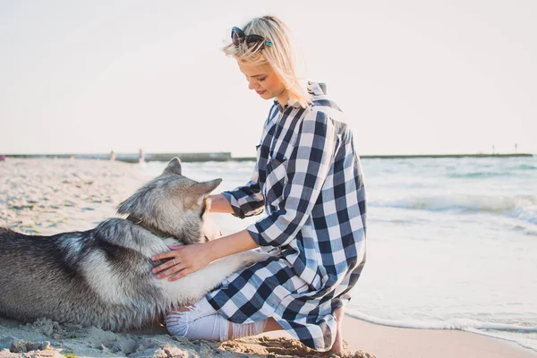 Молодая женщина обнимается с сибирской хаски-собакой на пляже на рассвете — стоковое фото