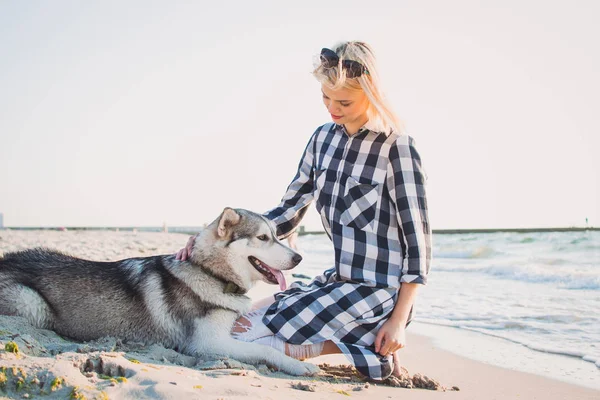 Jovem abraço feminino com cão husky siberiano na praia ao nascer do sol — Fotografia de Stock
