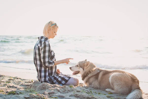 Jovem fêmea brincando com siberiano husky cão na praia ao nascer do sol — Fotografia de Stock