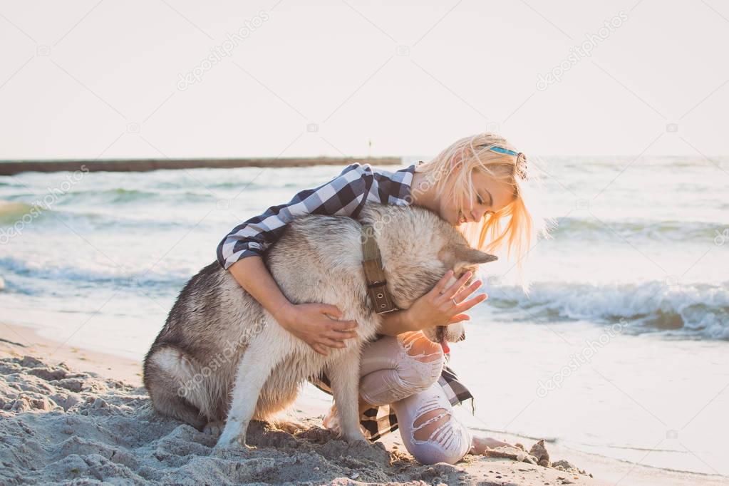 Young female hugging with siberian husky dog on the beach at sunrise