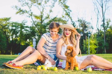 Parkta köpek ve tavşan ile yeşil Çimenlikte oturan genç çekici çift