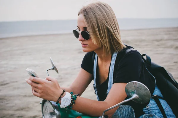 Young woman sitting at vintage scooter and using phone — Stock Photo, Image