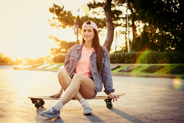 Dívka sedící na longboard v parku při východu nebo západu slunce — Stock fotografie