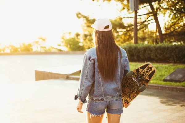 Chica joven con longboard caminando sola en el parque al amanecer o al atardecer — Foto de Stock