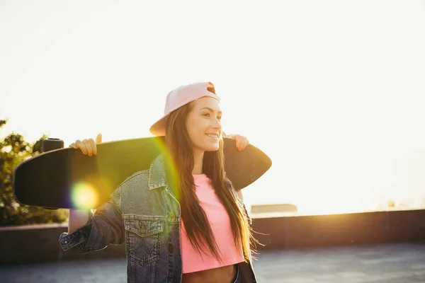 Menina com longboard de pé no parque ao nascer do sol ou pôr do sol — Fotografia de Stock