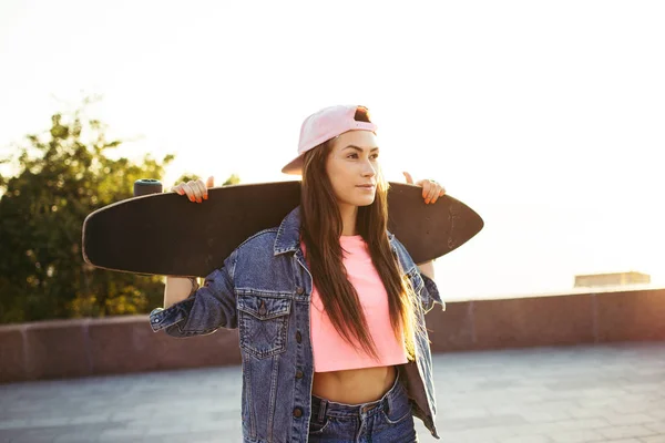 Menina com longboard de pé no parque ao nascer do sol ou pôr do sol — Fotografia de Stock