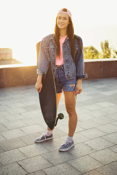 Menina com longboard de pé no parque ao nascer do sol ou pôr do sol — Fotografia de Stock