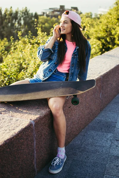 Menina sentada com longboard e falando ao telefone — Fotografia de Stock
