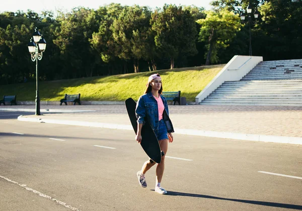 Menina com longboard andando sozinha no parque ao nascer ou ao pôr do sol — Fotografia de Stock