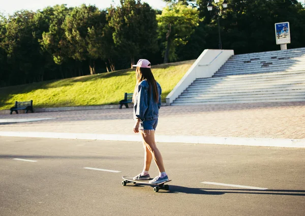 Chica joven montando longboard en el parque al amanecer o al atardecer — Foto de Stock