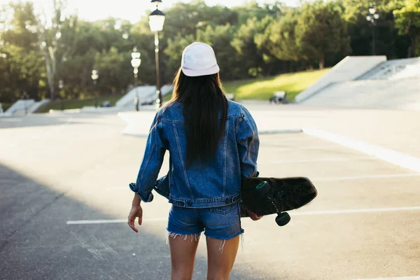 Young girl with longboard walking alone in the park at sunrise or sunset — Stock Photo, Image