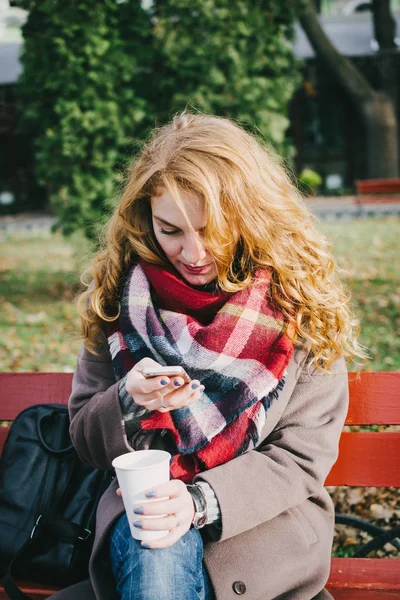 Young attractive woman sitting in the park and using phone — Stock Photo, Image