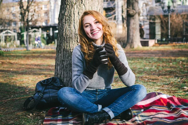 Νεαρή ευτυχισμένη γυναίκα κάθεται με ποτήρι του τσαγιού και χαμογελά στο πάρκο — Φωτογραφία Αρχείου