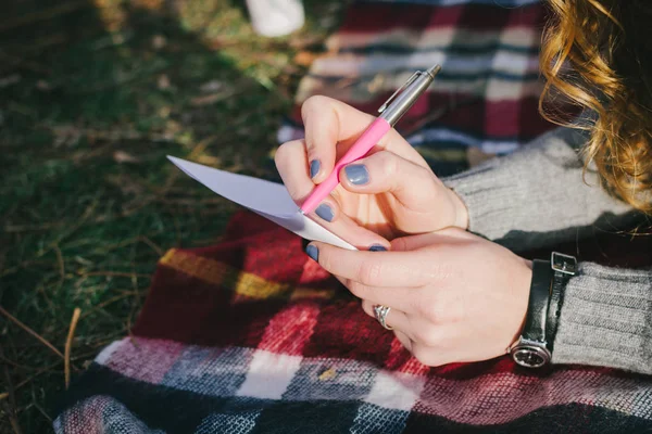 Young woman sitting and writing with pen at the checkered plaid, close up — Stock Photo, Image