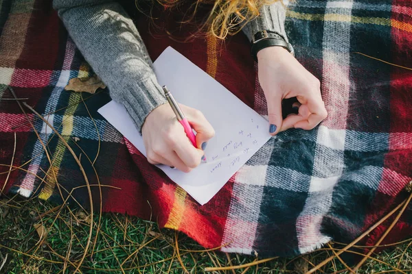 Young woman sitting and writing with pen at the checkered plaid, close up