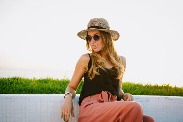 Mulher bonita em chapéu e óculos sorrindo e posando em frente ao mar — Fotografia de Stock