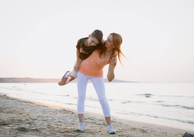 Anne ve oğlu gündoğumu veya günbatımı sırasında deniz sahilinde egzersiz yaparak