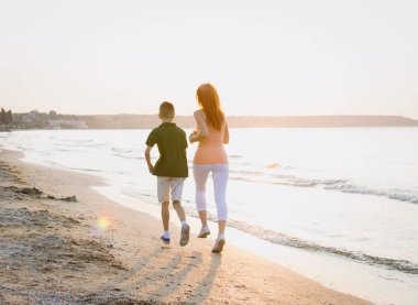 Anne ve oğlu deniz sahilinde gündoğumu veya günbatımı sırasında çalışan