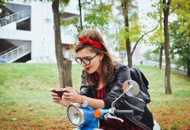 Mutlu genç hipster kadın akıllı telefon oyun parkı vintage onun scooter üzerinde