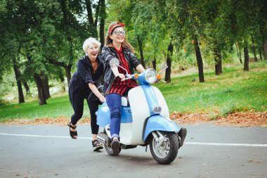 İki genç kadın parkta vintage scooter ile biraz eğlenmek