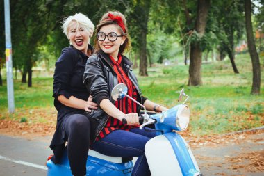 İki genç kadın parkta vintage scooter ile biraz eğlenmek