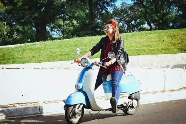 Счастливая молодая хипстерша в очках за рулем винтажного скутера в городе — стоковое фото
