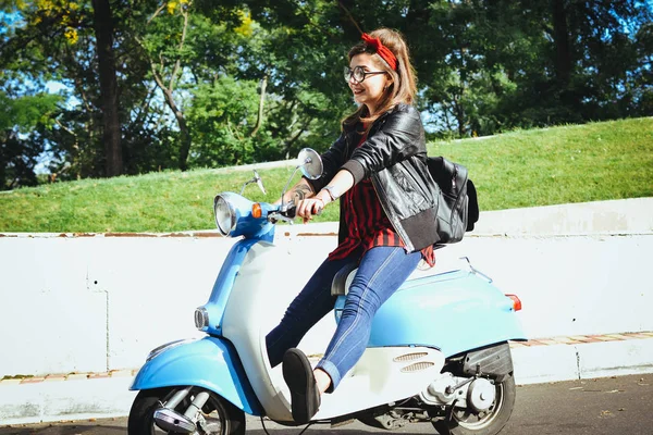 Mujer hipster joven feliz en gafas que conducen un scooter vintage en la ciudad — Foto de Stock