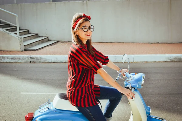 Happy young hipster woman in glasses driving a vintage scooter in city — Stock Photo, Image