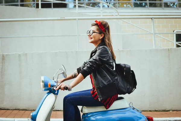 Feliz jovem hipster mulher em óculos dirigindo uma scooter vintage na cidade — Fotografia de Stock