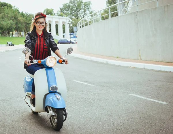 Feliz jovem hipster mulher em óculos dirigindo uma scooter vintage na cidade — Fotografia de Stock