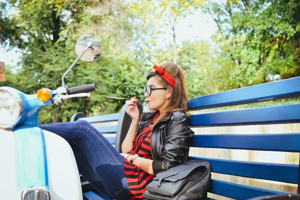 Jovem hipster mulher em óculos sentado em um banco e fumar cigarro — Fotografia de Stock