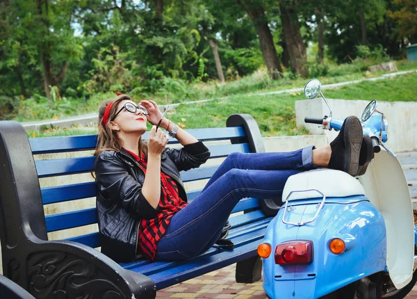 Jonge hipster vrouw in glazen zittend op een bankje en roken sigaret — Stockfoto