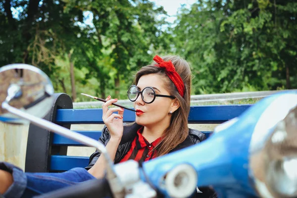 Молода хіпстерка в окулярах сидить на лавці і курить сигарету — стокове фото